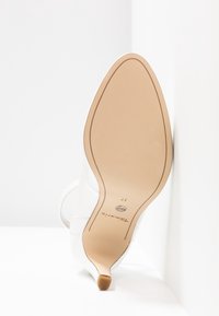 Semelle d'une chaussure à talon haut blanche à bout pointu, taille 37, avec semelle beige et petit embout de talon, photographiée sur fond blanc.