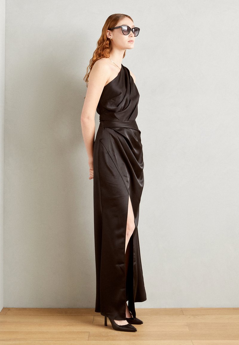 Melna satīna kleita ar vienu plecu, plūstošs dizains, augsts sānu izgriezums, stilizēta ar melnām augstpapēžu kurpēm un saulesbrillēm. Gluda tekstūra.