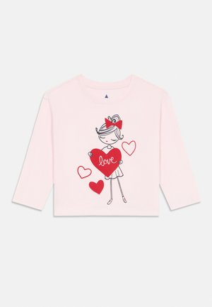 Roze shirt met lange mouwen met een illustratie van een meisje dat een rood hart vasthoudt met het woord "liefde", omringd door drie kleinere rode en witte harten.