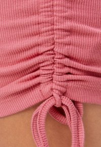 Růžová žebrovaná látka s nařasením a zavazováním. Textura je měkká s viditelným švem a jemným pružením.