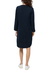 Granatowa sukienka do kolan z długimi rękawami i okrągłym dekoltem, wykonana z miękkiego materiału. Posiada zaokrąglony dół i mankiety przy nadgarstkach.