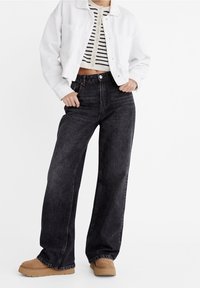 Jeans de mezclilla negros de pierna ancha con una cintura alta, combinados con un suéter recortado a rayas en blanco y negro y botas de plataforma color beige.