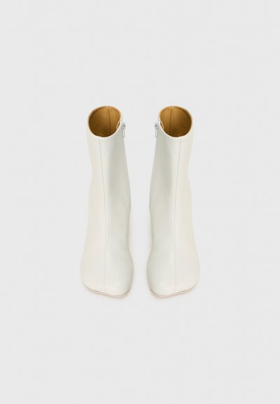 Bottes de cheville en cuir blanc avec une texture lisse, un bout pointu et un design minimaliste. Dotées d'une fermeture éclair sur le côté et d'un intérieur beige.