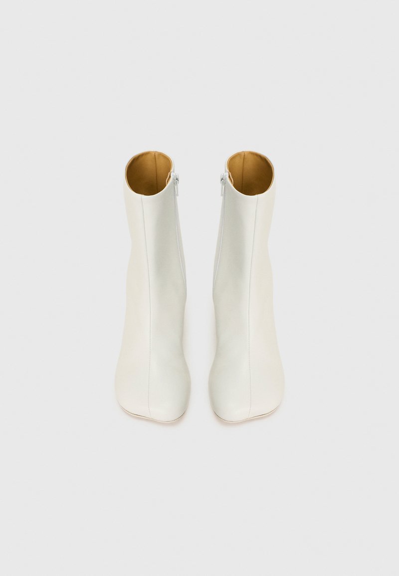 Stivali alla caviglia bianchi in pelle con texture liscia, punta affusolata e design minimalista. Presentano una zip laterale e un interno beige.