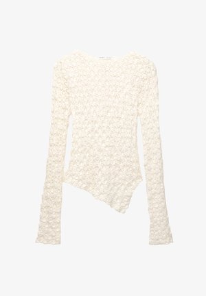 Valkoinen pitkähihaisen neulepusero, jossa on kukkakuosi ja epäsymmetrinen helma.