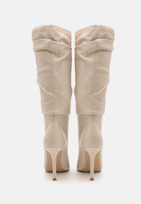Béžové vysoké boty do kolen vyrobené z hladké kůže, se sklopeným designem a stiletto podpatky, s čistou a minimalisticou estetikou.