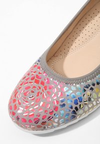 Ballerines grises avec un motif perforé multicolore et semelle intérieure beige rembourrée visible à l'intérieur de la chaussure.
