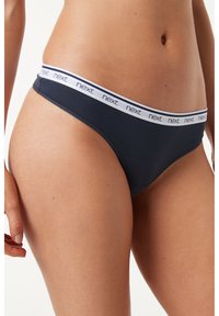 String noir avec une ceinture élastique blanche portant le nom de la marque "next" répété. Texture de tissu lisse avec un design minimal.