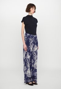 Navy mock-neck top paired with wide-legged, floral-patterned trousers in cream and blue. Model stands in flat shoes against a plain background.