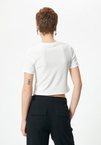 Hvid cropped t-shirt med korte ærmer, glat tekstur, rund halsudskæring, parret med højtaljede sorte bukser med baglommer.