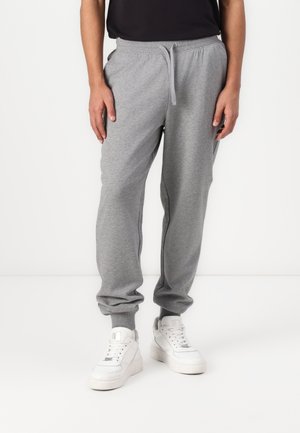 Graue Jogginghosen mit elastischem Bund und Bündchen, ausgestattet mit seitlichen Taschen. Kombiniert mit weißen Sneakers, auf einem schlichten Hintergrund.