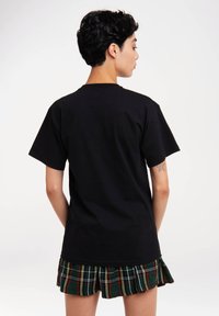 Schwarz Baumwoll-T-Shirt mit kurzen Ärmeln, Rundhalsausschnitt und lockerer Passform, kombiniert mit einem grünen karierten Faltenrock.