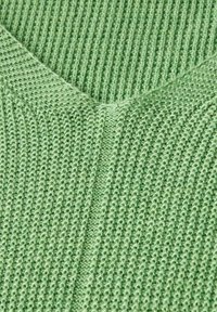 Jasnozielona dzianina z dekoltem w serek, charakteryzująca się teksturowanym wzorem. Materiał ma miękki, prążkowany wygląd, z kontrastującym przeszyciem.