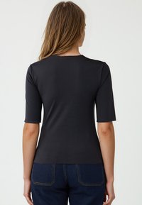 Zwarte korte mouw top met een gladde textuur, ronde halslijn en een aansluitend ontwerp, gecombineerd met donkerblauwe denim jeans.