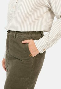 Gestreepte beige blouse met knoopdetails gecombineerd met een olijfgroene corduroy rok met zijzakken en een elastische tailleband.