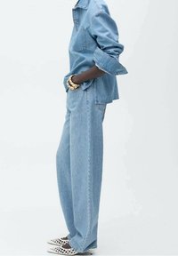 Jasnoniebieska dżinsowa kurtka z kieszonką, w połączeniu z luźnymi jasnoniebieskimi dżinsami. W zestawie białe, wzorzyste obuwie oraz złota bransoletka.