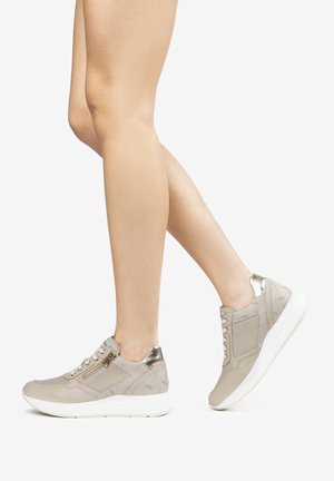 Zapatillas beige con parte superior texturizada, acentos metálicos y suela blanca. Presentan cordones y un detalle de cremallera lateral.