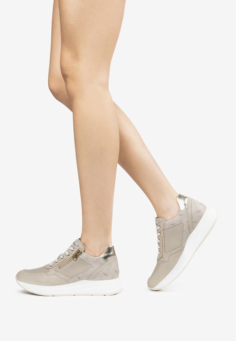 Zapatillas beige con parte superior texturizada, acentos metálicos y suela blanca. Presentan cordones y un detalle de cremallera lateral.