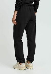 Sorte sweatpants med elastisk talje og samlet manchetter, lavet af blødt stof. Parret med lysfarvede, polstrede sneakers.