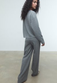 Sivý loungewear set s voľným strihom a dlhým rukávom, a nohavicami s širokými nohavicami, vyrobený z mäkkej látky s hladkou textúrou.