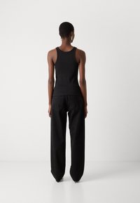 Svart ribbad tanktopp med fitted design, tillsammans med lösa svarta jeans med hög midja och rak benpassform, sett bakifrån.