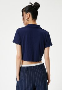 Marineblaue, kurz geschnittene Polohemd mit gerippter Textur und gewelltem Saum, kombiniert mit marineblauen gestreiften Hosen und elastischem Bund.
