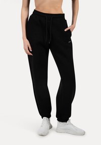 Sorte joggingbukser lavet af blødt stof med elastisk talje, justerbar snor og sidelommer. Enkelt design uden mønstre.