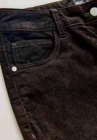 Schwarze Cordhosen mit weicher Textur, die über eine Vordertasche, einen weißen Metallknopf und kontrastierende Nähte verfügen.