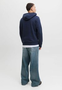 Marineblauer Hoodie mit Kordelzug, gerippten Bündchen und Saum, kombiniert mit hellblauen weit geschnittenen Jeans mit Gesäßtaschen und verwaschenem Stoff.