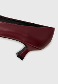 Décolleté in pelle borgogna con punta arrotondata e tacco nero sottile. Texture liscia con dettagli di cucitura discreti lungo il bordo.
