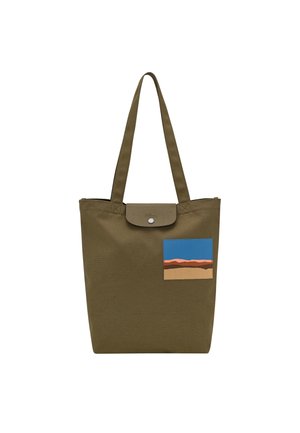 Olive green tote bag with long straps and front landscape patch featuring blue sky and brown hills, snap button flap closure.