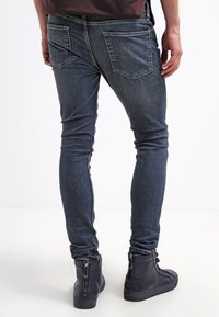 Vaqueros de mezclilla oscura de corte ajustado, con bolsillos traseros y lavado desteñido. Combinados con botas negras altas con detalle de cremallera.