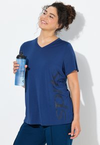 Krátké tmavě modré tričko s výstřihem do V a texturovaným grafickým potiskem po straně. Model drží světle modrou lahev na vodu.