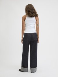 Jeans largas de cor azul-escuro com a bainha dobrada em tecido cinza. Combinadas com um top justo branco sem mangas, vistas de costas.