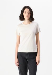 Light beige short-sleeve t-shirt with a round neckline and soft texture, displayed with black high-waisted jeans.