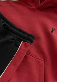 Bordeaux sweatshirt med kængurulomme og lille sort hjortelogo, parret med sorte sweatpants, der har bordeaux side-striber og hvid piping.