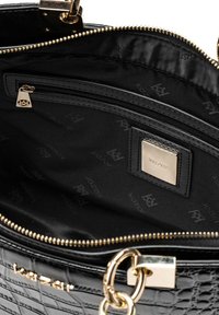 Mustan krokotiilikuviollisen laukun sisäosa, jossa on kultainen vetoketju, kangasvuori, vetoketjullinen tasku ja kultainen logokilpi. Pinta on sileä.