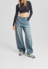 Jeans in denim azzurro chiaro a gamba larga con vita alta e tasche frontali; abbinati a un top attillato a coste con maniche lunghe di colore scuro.