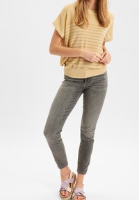 Jasnożółta dzianinowa bluzka w poziome paski, zestawiona z jasnoszarymi dopasowanymi jeansami oraz beżowymi sandałami na platformie z lawendowymi paskami.