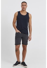 Maglietta senza maniche blu navy con scollo a girocollo, abbinata a shorts di denim grigio scuro strappati e sneakers nere. Design semplice e vestibilità casual.