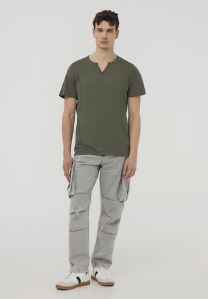 T-shirt verde oliva a maniche corte con scollatura a V e dettaglio a due bottoni, abbinato a pantaloni cargo grigi con tasche laterali e una vestibilità morbida.