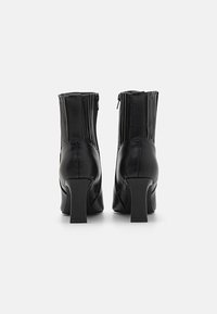 Bottines en cuir noir avec un design élégant, dotées d'un talon bloc haut et de plis verticaux à l'arrière, avec une fermeture éclair.