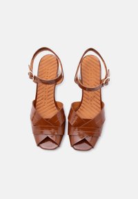 Καφέ παπούτσια με λουριά από δερμάτινο γυαλιστερό ύφασμα, ψηλοτάκουνα σανδάλια με σταυρωτά λουριά, ανοιχτή μύτη, λουράκι στον αστράγαλο και ανάγλυφη εσωτερική σόλα με ριγέ σχέδιο.