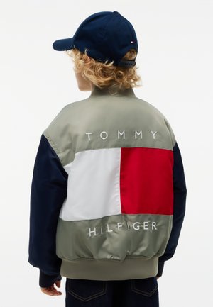 Enfant aux cheveux bouclés portant une casquette bleue et une veste color block Tommy Hilfiger avec logo dans le dos, de dos.