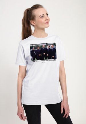 Kvinde med langt hår samlet i hestehale iført hvid T-shirt med fem mænd i jakkesæt fra The Sopranos og citattekst nedenunder.