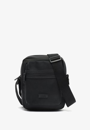 Kompakte schwarze Umhängetasche mit vorderer Reißverschlusstasche und verstellbarem Schulterriemen, gefertigt aus strukturiertem synthetischem Material.