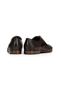 Un paio di scarpe da uomo in pelle marrone scuro con texture, con tacchi in legno, viste da dietro su sfondo bianco.