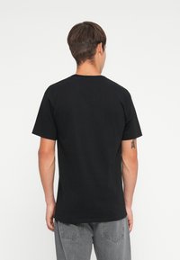 Black cotton t-shirt with a crew neckline and short sleeves, viewed from the back, paired with light gray denim jeans.