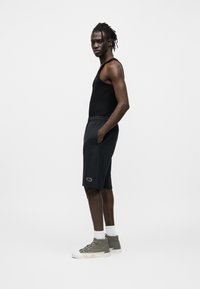 Μαύρο αμάνικο τοπ, γκρι σορτσάκια με πλαϊνές τσέπες και παπούτσια υψηλού κορμού. Απλά χρώματα, casual σχεδιασμός και απλή σήμανση στα σορτσάκια.