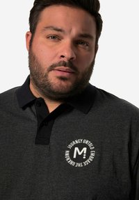 Tmavě šedé polo tričko s černým límečkem, zdobené bílým kruhovým logem a textem. Tkanina vypadá měkká, s knoflíkovou légou.